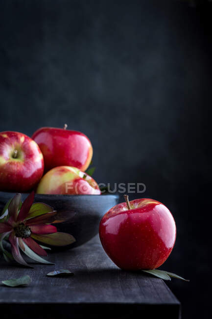 Manzanas rojas frescas sobre mesa de madera y en un bol sobre fondo oscuro. - foto de stock