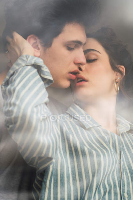 Sensual joven hombre y mujer besándose detrás de la ventana - foto de stock