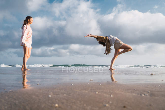 Female friends doing exercises on beach under cloudy sky — Stock Photo