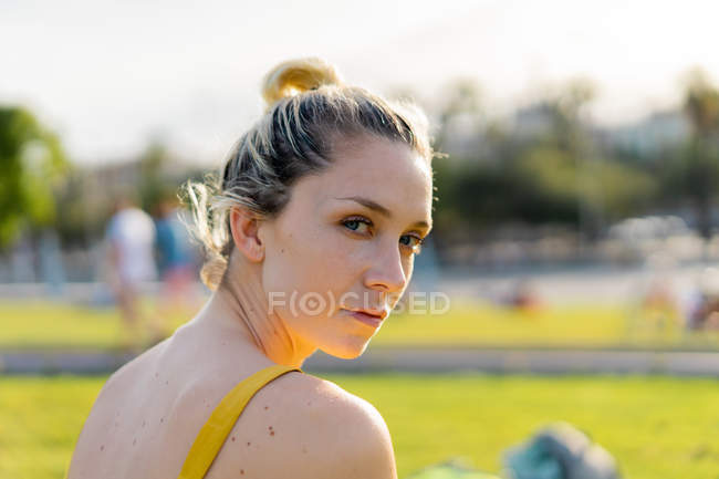 Mulher sentada na grama no parque e olhando sobre o ombro — Fotografia de Stock