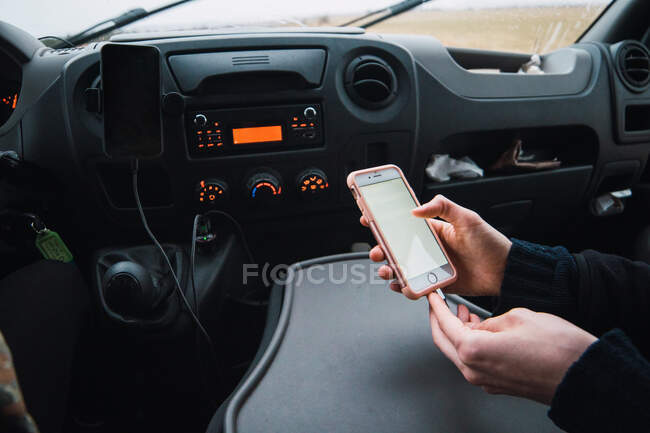 Schnappschuss von Frau auf Beifahrersitz im Auto, die während der Fahrt Smartphone mit Kabel auflädt. — Stockfoto