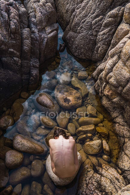 Vista superior de la mujer desnuda sentada en piedras y tocando de nuevo en el agua en la naturaleza. - foto de stock