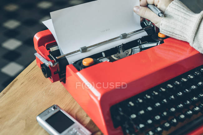 Cellulare e macchina da scrivere rossa brillante con penna a mano umana — Foto stock