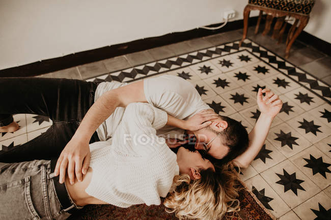 Feliz hombre y mujer acostados en el suelo y besándose en casa - foto de stock