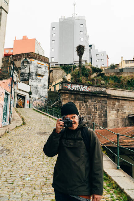 Fotógrafo alegre homem com câmera em pé na rua da antiga cidade europeia. — Fotografia de Stock