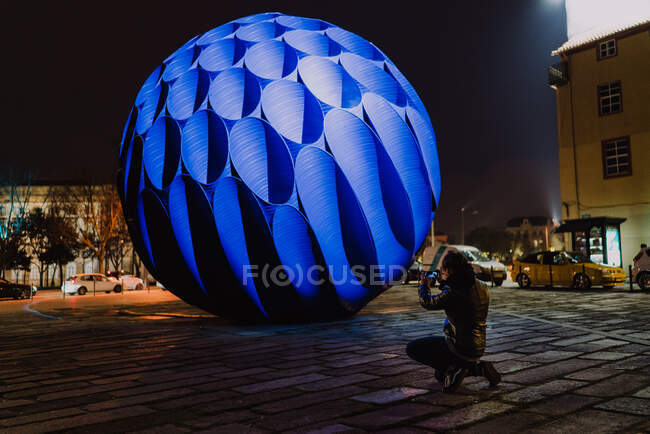Grand monument de sphère bleue illuminé la nuit et photographe prenant des spectacles. — Photo de stock