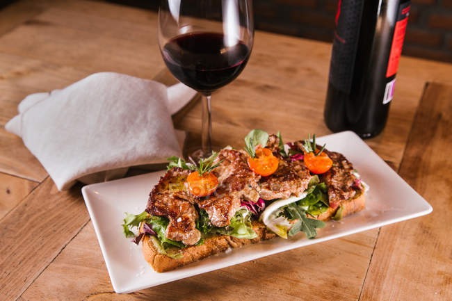 Sandwich avec viande et légumes frits et verre de vin rouge sur table en bois — Photo de stock