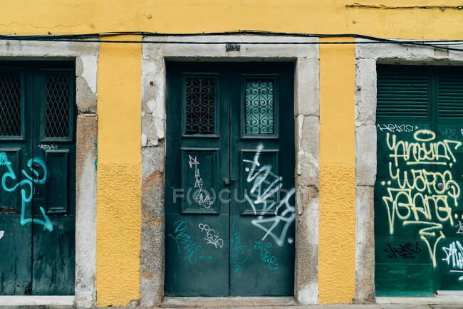 Portas verdes velhas com etiquetas de grafite no edifício amarelo. — Fotografia de Stock
