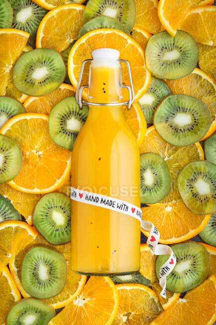 Von oben Flasche handgemachten Saft auf Muster von Kiwis und Orangenstücken. — Stockfoto