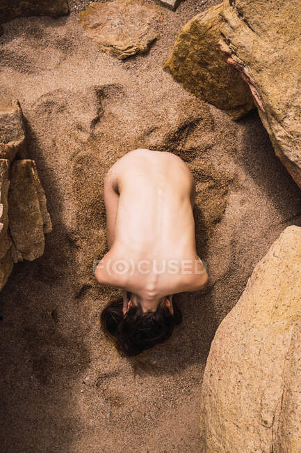 Desde arriba mujer desnuda irreconocible acostada en la arena en las rocas. - foto de stock