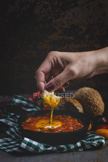 Людська рука над смаженим яйцем з помідорами, червоним перцем і хлібом на сковороді — стокове фото