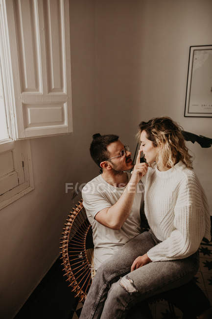 Man sitting in armchair and touching nose of girlfriend at home — Stock Photo