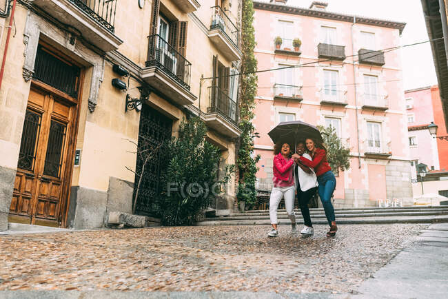 Grupo de três belas mulheres multirraciais jovens se divertindo andando sobre a chuva — Fotografia de Stock