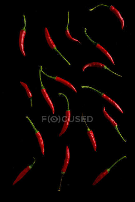 Red chili peppers scattered on black background — Stock Photo