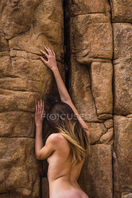 Vue arrière de la femme nue grimpant sur un mur de montagne rugueux. — Photo de stock