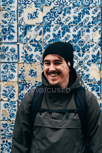 Homme touristique joyeux debout au mur avec des tuiles bleues — Photo de stock