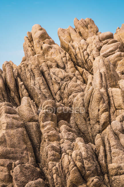 Снизу грубая скала с камнями на вершине и облачным голубым небом. — стоковое фото