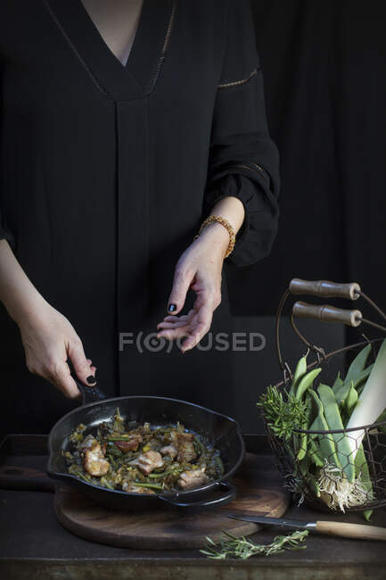 Crop unrecognizable cook putting rosemary to pan with cooking food. — Stock Photo