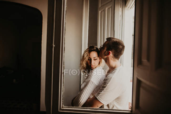 Pareja romántica abrazándose en la ventana en casa - foto de stock