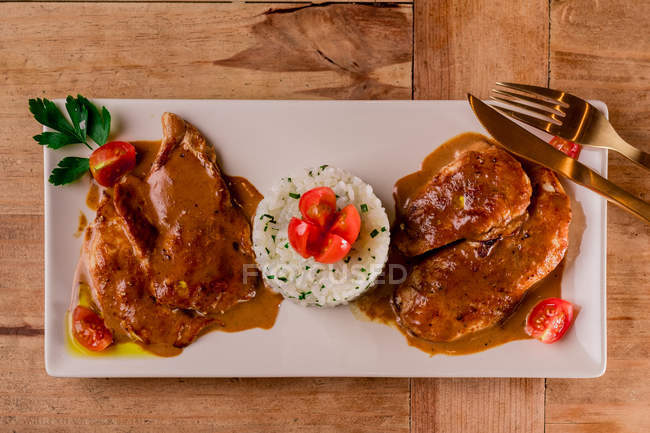 Смажене м'ясо з соусом та рисом на білій тарілці з виделкою та ножем — стокове фото