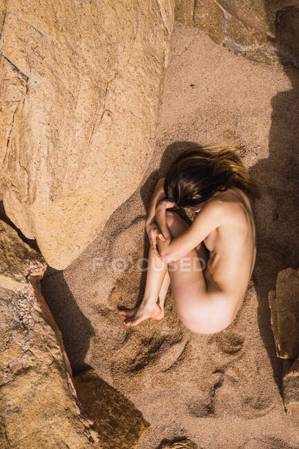 Dall'alto donna nuda irriconoscibile sdraiata sulla sabbia nelle rocce. — Foto stock