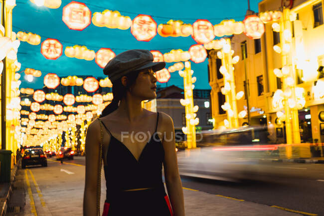 Mulher asiática jovem na moda olhando para longe na cidade iluminada à noite. — Fotografia de Stock