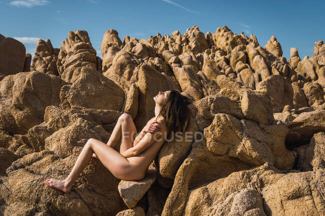 Vue latérale de la femme nue ajustant les cheveux et assise sur le rocher. — Photo de stock