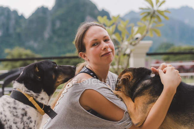 Erwachsene Frau schaut beim Streicheln und Spielen mit Hunden in der Natur in die Kamera. — Stockfoto