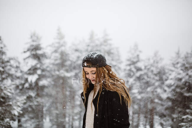 Vista lateral da mulher bonita de pé e olhando para a câmera na estrada em queda de neve. — Fotografia de Stock