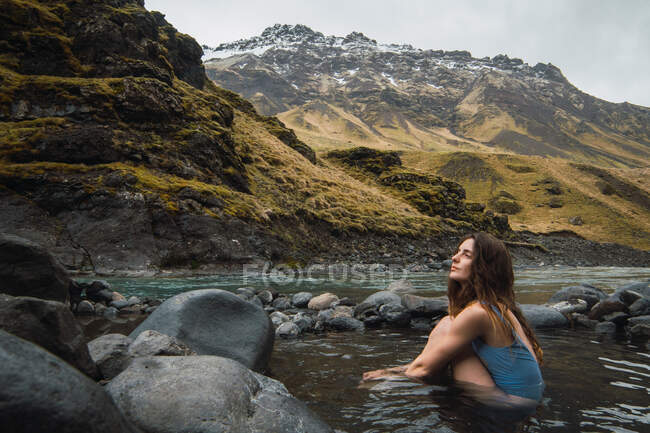 Молода жінка сидить у гірській річці — стокове фото