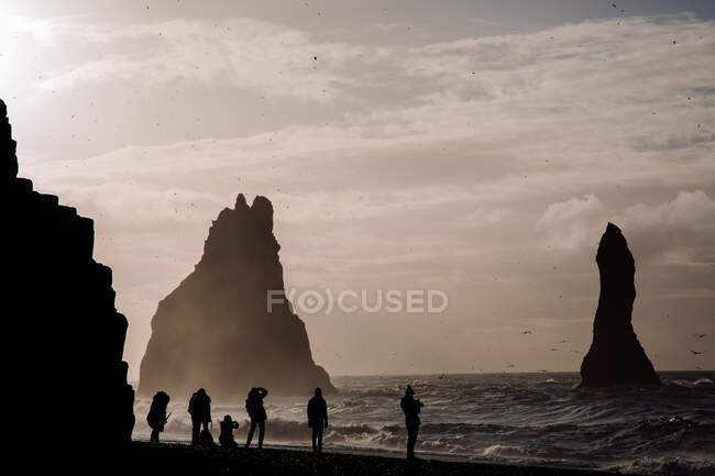 Grupo de turistas irreconhecíveis na costa oceânica com grandes rochas na Islândia. — Fotografia de Stock