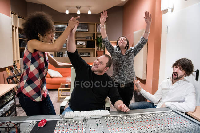 Grupo de personas regocijándose por el éxito y divirtiéndose después de grabar música en el estudio - foto de stock