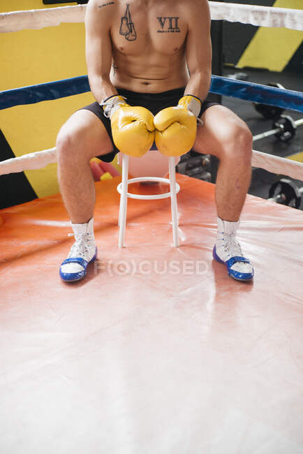 Shirtless confident boxer in gloves sitting on stool in the ring. — Stock Photo