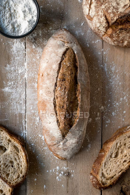 Loaf of rye bread covered with flour on wooden table — Stock Photo