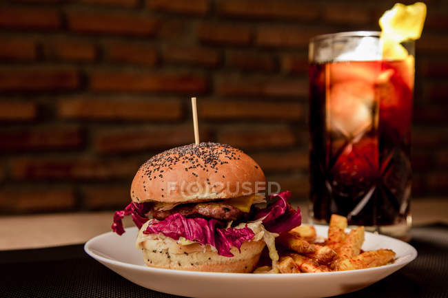 Вкусный бургер с картошкой фри на тарелке и стаканом кокаина — стоковое фото