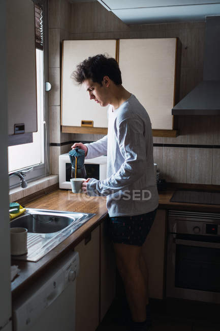 Человек в пижаме наливает кофе в чашку на кухне — стоковое фото