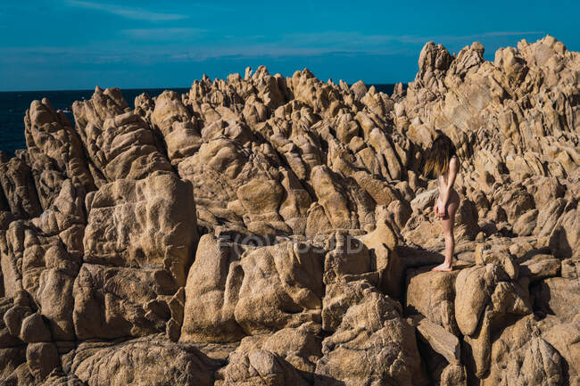 Side view of unrecognizable attractive nude woman standing on rock in sunny day. — Stock Photo