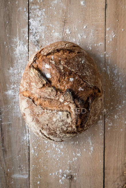 Circle-shape loaf of rye bread on wooden table with flour — Stock Photo