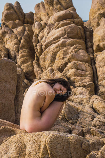 Боковой вид неузнаваемой обнаженной девушки, сидящей на камнях и отводившей взгляд. — стоковое фото