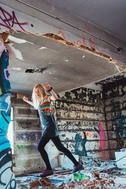 Junges Mädchen in hellem Outfit balanciert auf zerbrochenen Ziegeln und Müll in farbig verlassenem Raum. — Stockfoto