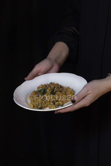 Manos de cocinero irreconocible sosteniendo plato con risotto. - foto de stock