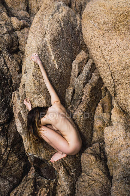 Seitenansicht einer nicht wiederzuerkennenden heißen nackten Frau, die auf einem Felsen sitzt und hält. — Stockfoto