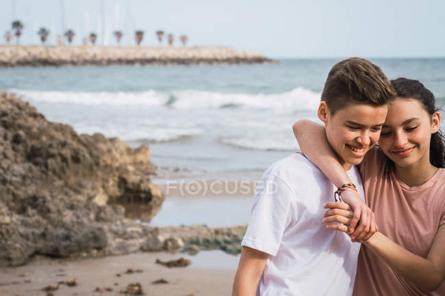 Sonrisa adolescente chica y chico de pie en la playa - foto de stock