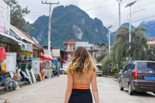 Vue arrière de la femme debout sur la route asphaltée dans le village. — Photo de stock