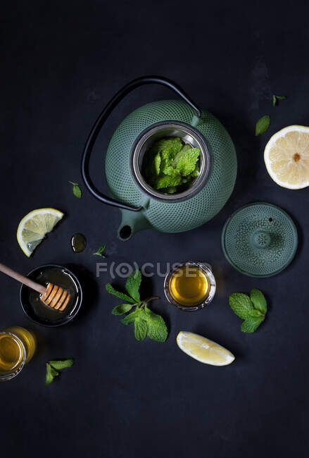 Du dessus de la théière avec des feuilles fraîches et du citron sur la table. — Photo de stock