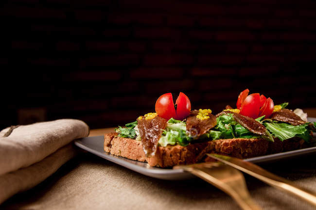 Сендвіч з овочами та рибою на сірій тарілці на дерев'яному столі — стокове фото