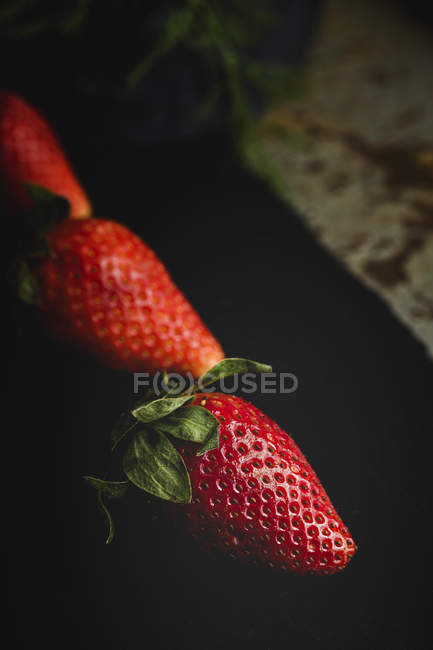 Gros plan de délicieuses fraises texturées sur une surface noire — Photo de stock
