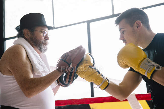 Vista lateral do boxeador luvas de perfuração do treinador no ginásio. — Fotografia de Stock