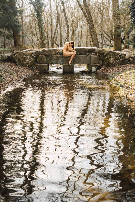 Naked lady on bridge in autumn forest in pose above river copy space — Stock Photo
