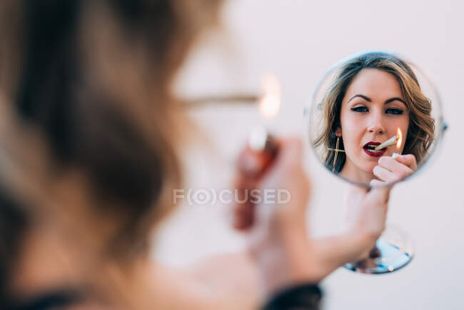 Young woman smoking a cannabis joint in the mirror — Stock Photo